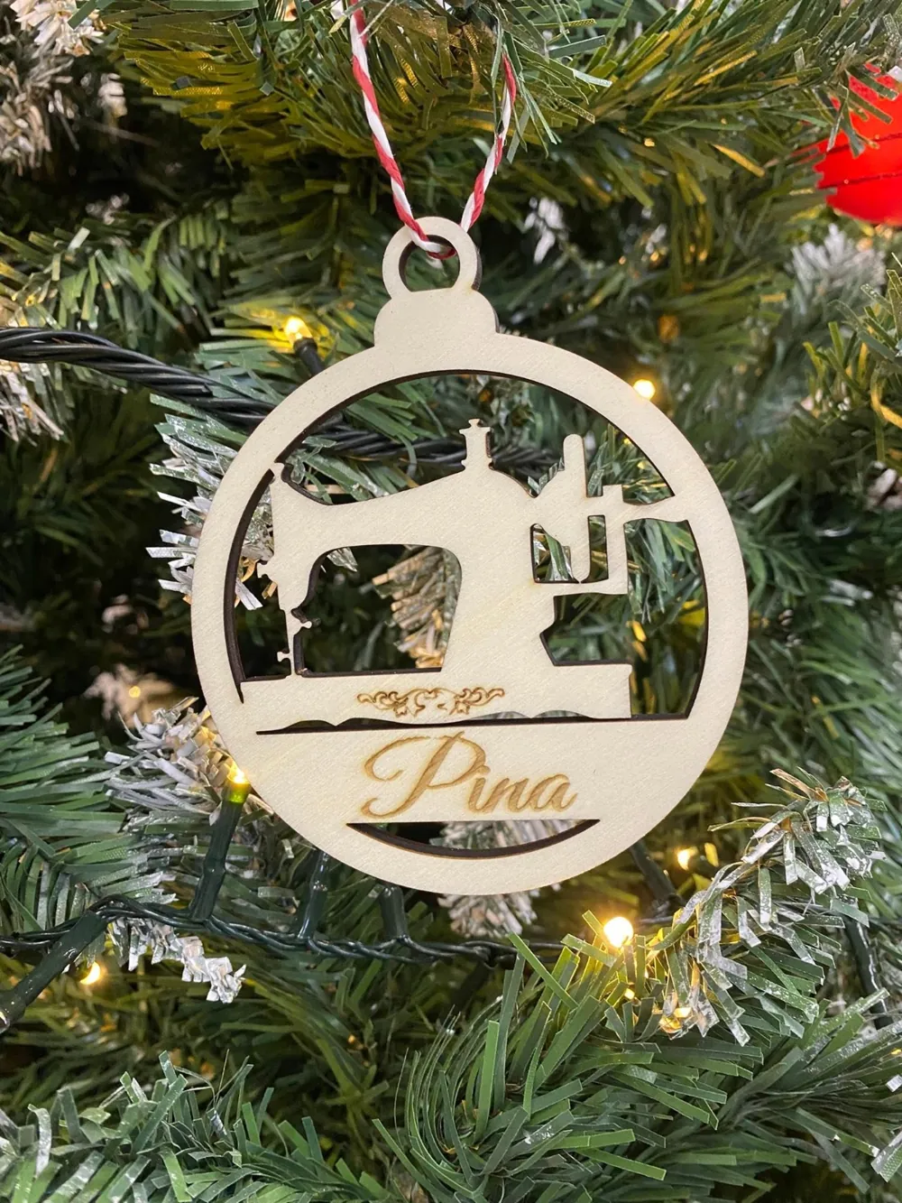 Pallina di Natale in legno con la macchina da cucire traforata e il nome Pina, appesa all'albero