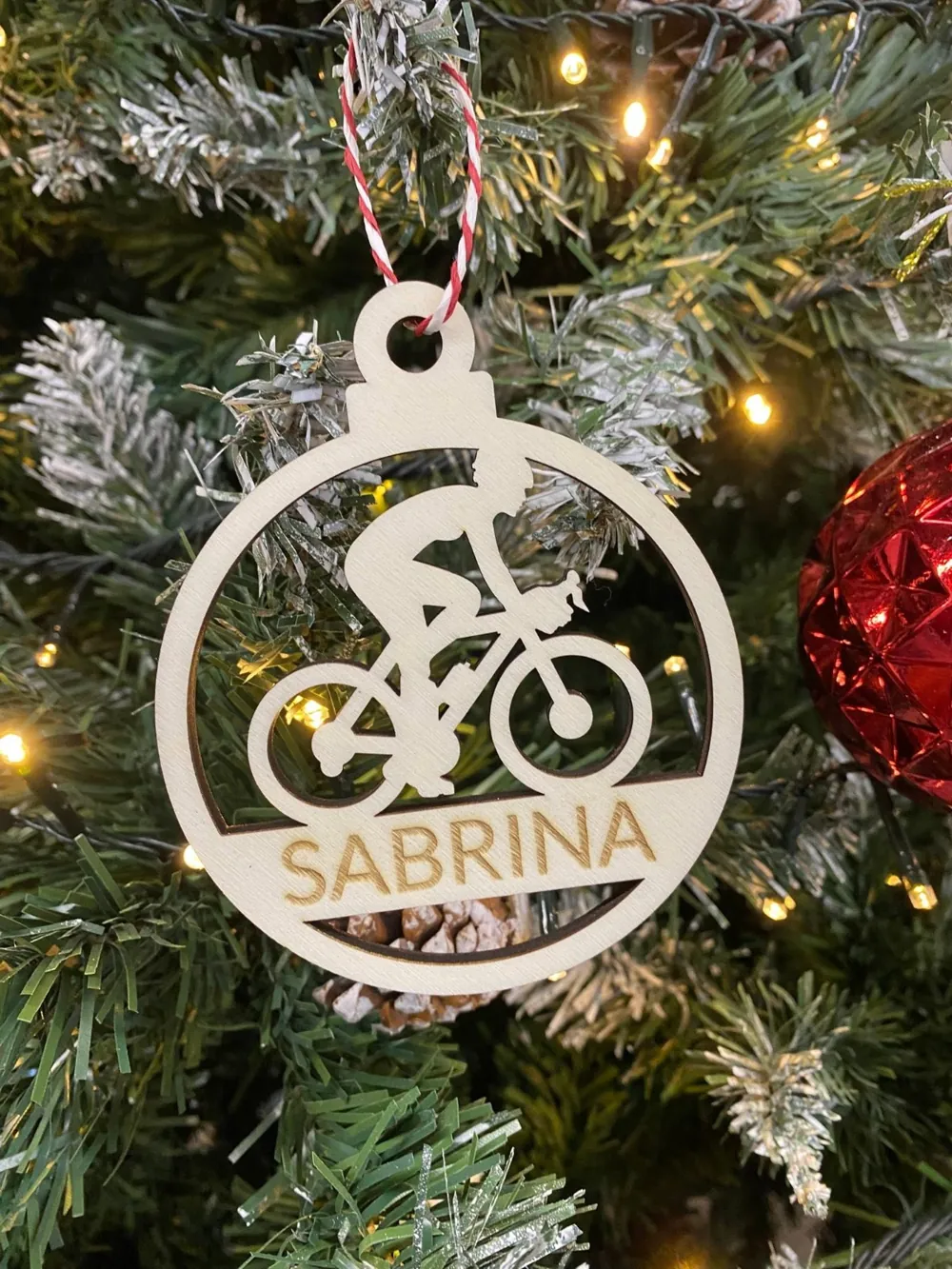 Pallina di Natale in legno con un ciclista traforato e il nome Sabrina, appesa all'albero