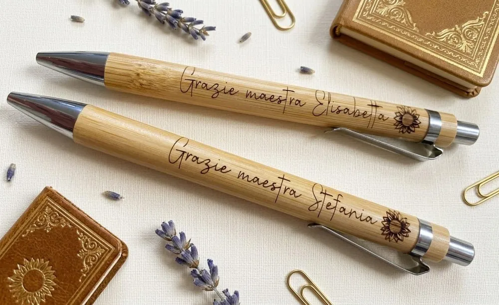 Due penne di bambù incise con la dedica Grazie maestra e un girasole